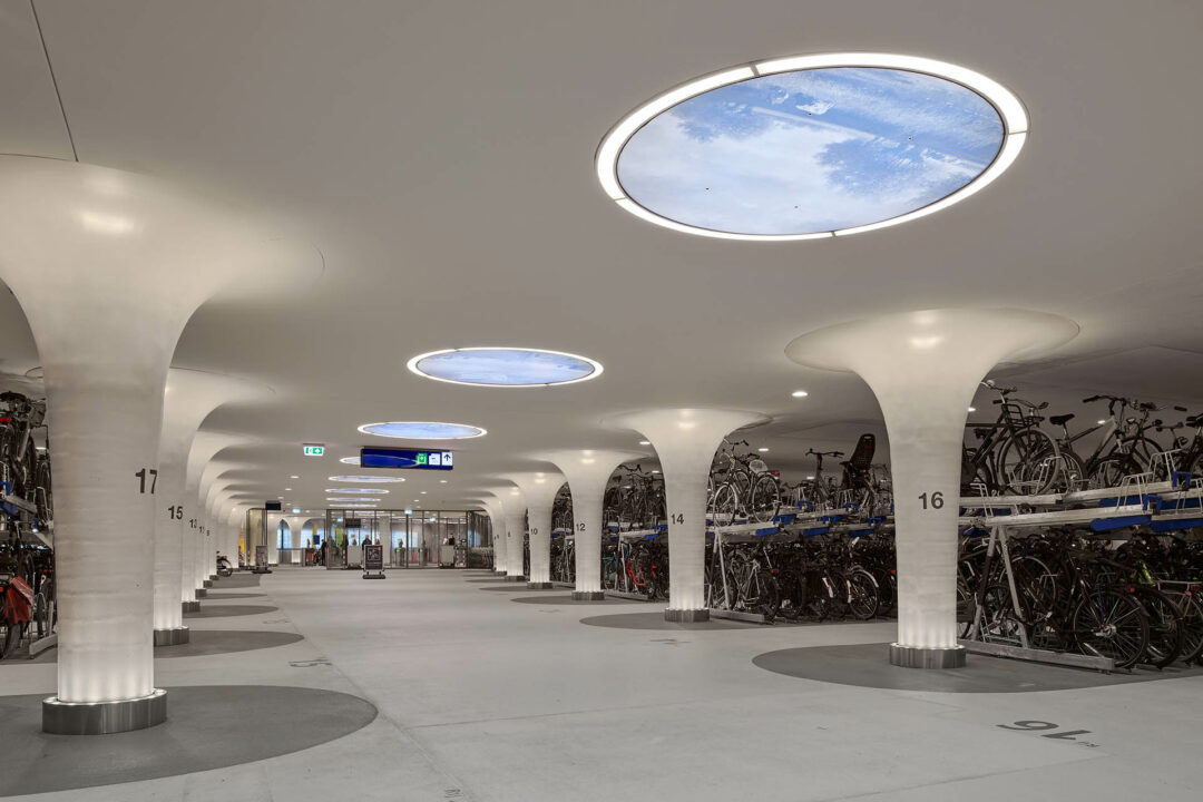 Een foto van grote ronde lichten (oculi) aan het plafond van de ondergrondse fietsenstalling.